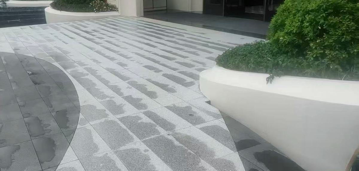Two-tone flamed grey granite paving at a building entrance plaza, laid in light and dark bands with a curved dark inlay