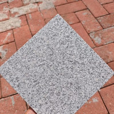 Hand holding a 100 mm flamed G603 granite sample tile